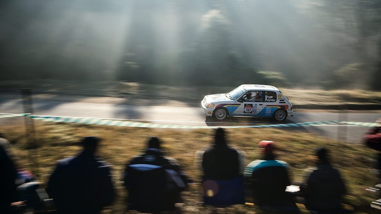 Auto de rally circulando por una ruta ante un grupo de espectadores