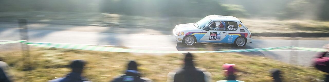 Auto de rally circulando por una ruta ante un grupo de espectadores