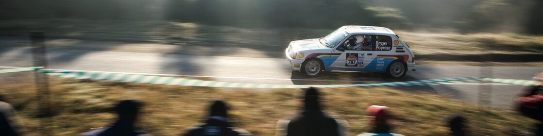 Auto de rally circulando por una ruta ante un grupo de espectadores