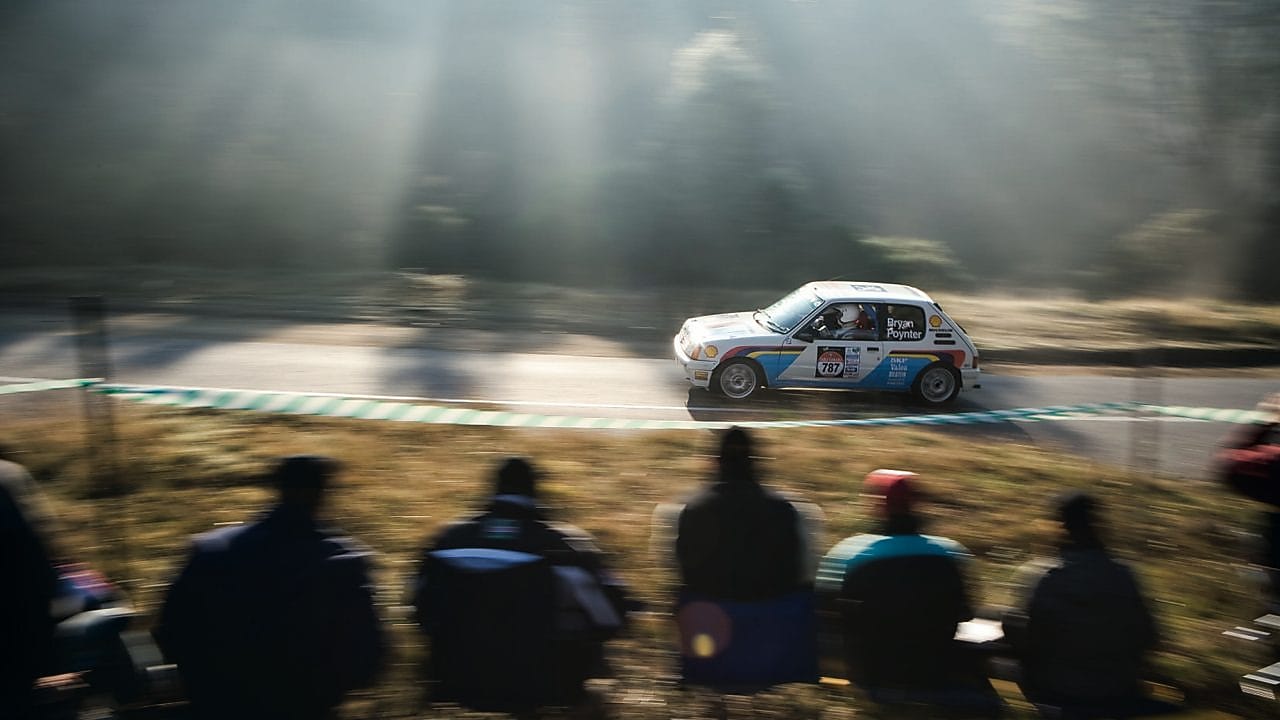 Auto de rally circulando por una ruta ante un grupo de espectadores