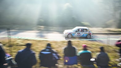 Auto de rally circulando por una ruta ante un grupo de espectadores