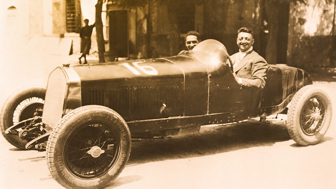 Fotografía en blanco y negro de Enzo Ferrari sentado en uno de sus primeros autos Ferrari