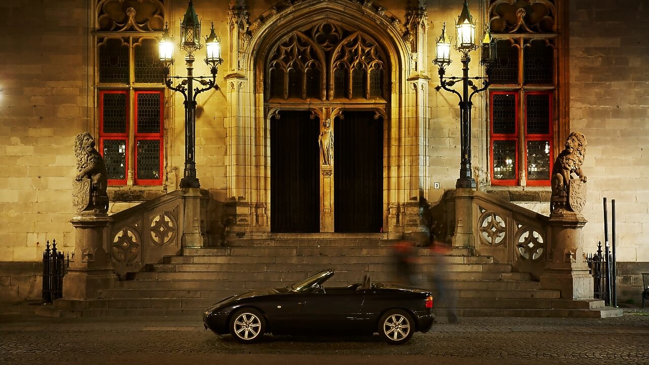 Auto negro estacionado de noche en el exterior de una casa grande, junto a unos escalones de piedra