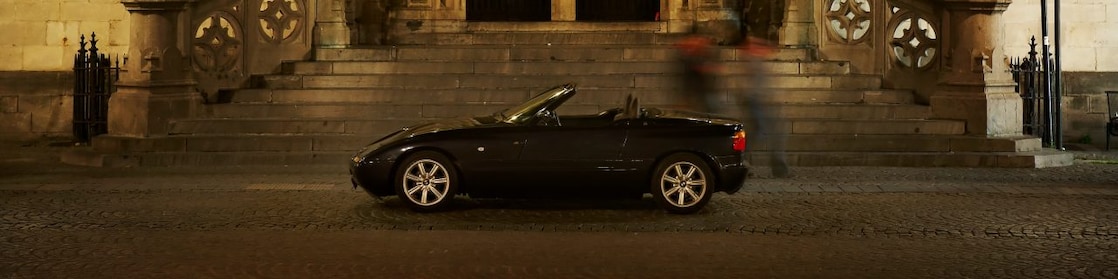 Auto negro estacionado de noche en el exterior de una casa grande, junto a unos escalones de piedra