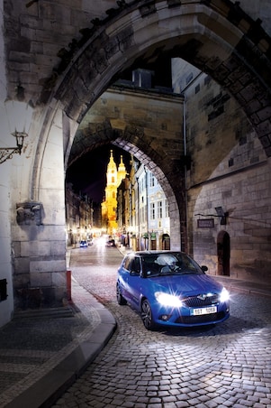 Auto azul aparcado bajo un arco en una calle empedrada de Praga de noche