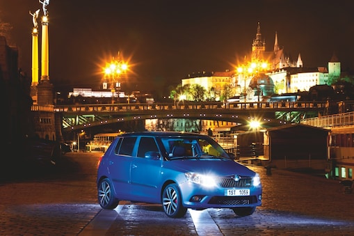 Auto azul estacionado en una calle de Praga con un puente y el castillo al fondo, de noche
