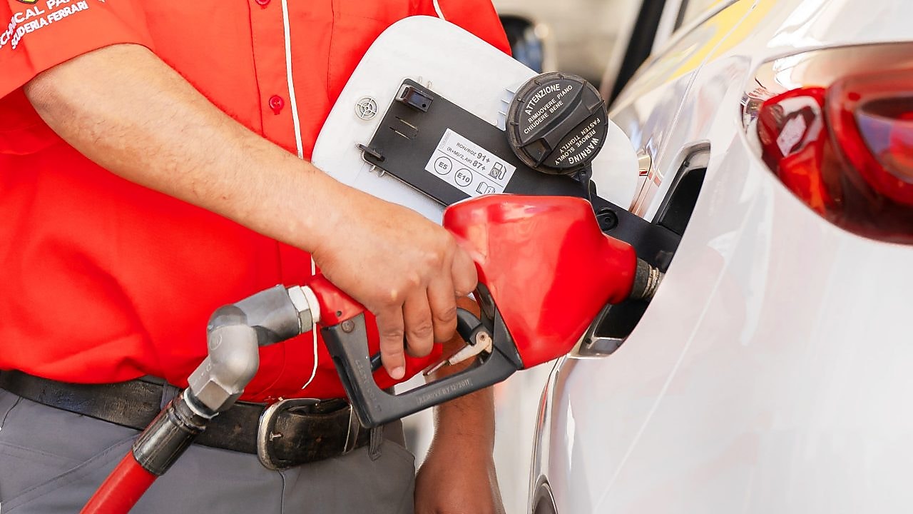 Hombre manejando un vehículo por una carretera larga rodeada de árboles.