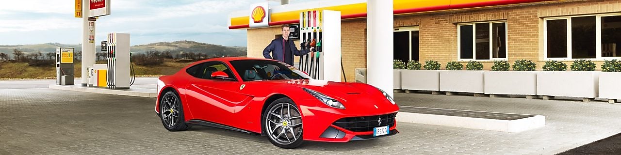 Ferrari rojo en una estación de servicio Shell con un hombre apoyado sobre un surtidor