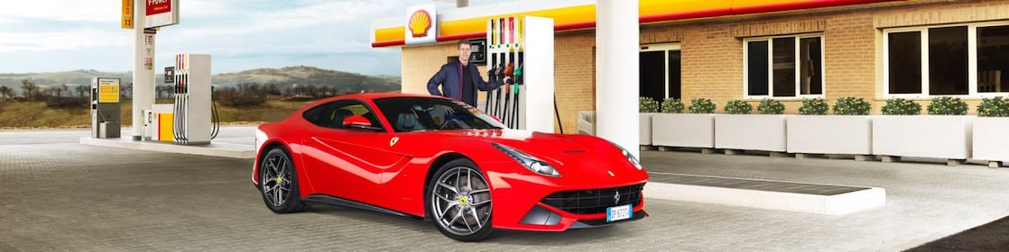 Ferrari rojo en una estación de servicio Shell con un hombre apoyado sobre un surtidor