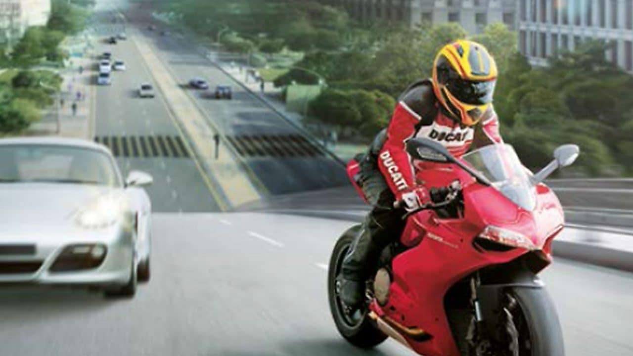 Motocicleta roja y piloto en una ruta con autos y edificios en el fondo