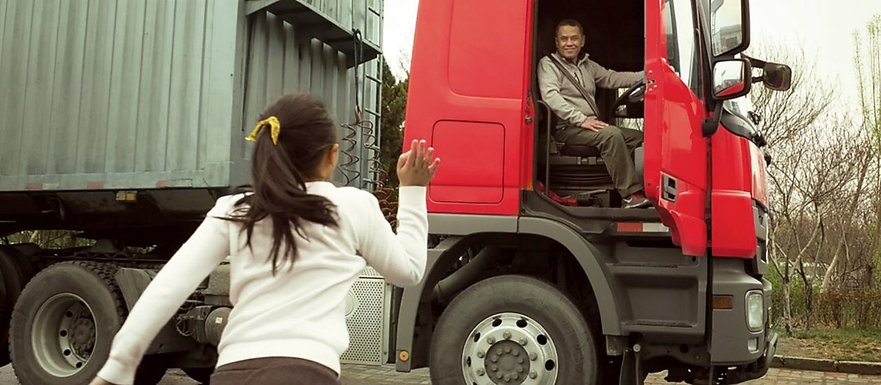Hombre en una cabina roja de camión con la puerta abierta despidiéndose de su hija