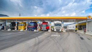 Gasolinera Shell con seis camiones aparcados. De izquierda a derecha: un camión blanco, verde oscuro, amarillo, azul oscuro, rojo y otro camión blanco.