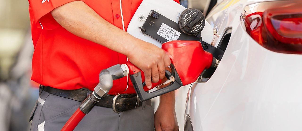 Hombre manejando un vehículo por una carretera larga rodeada de árboles.